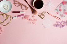 coffee cup, makeup, and earrings on a pink background 