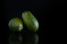 two whole avocados with reflection and copy space on a black background