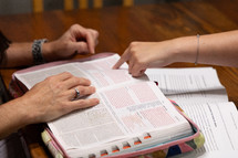 Two young women studying Bible during discipleship group Bible study, pointing to verse