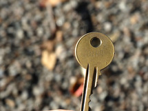  Close up of golden round key with number imprinted on it, gravel background