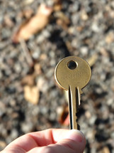 Close up of golden round key with number imprinted on it, gravel background