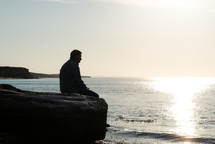 a man sitting on rocks thinking at the coast 