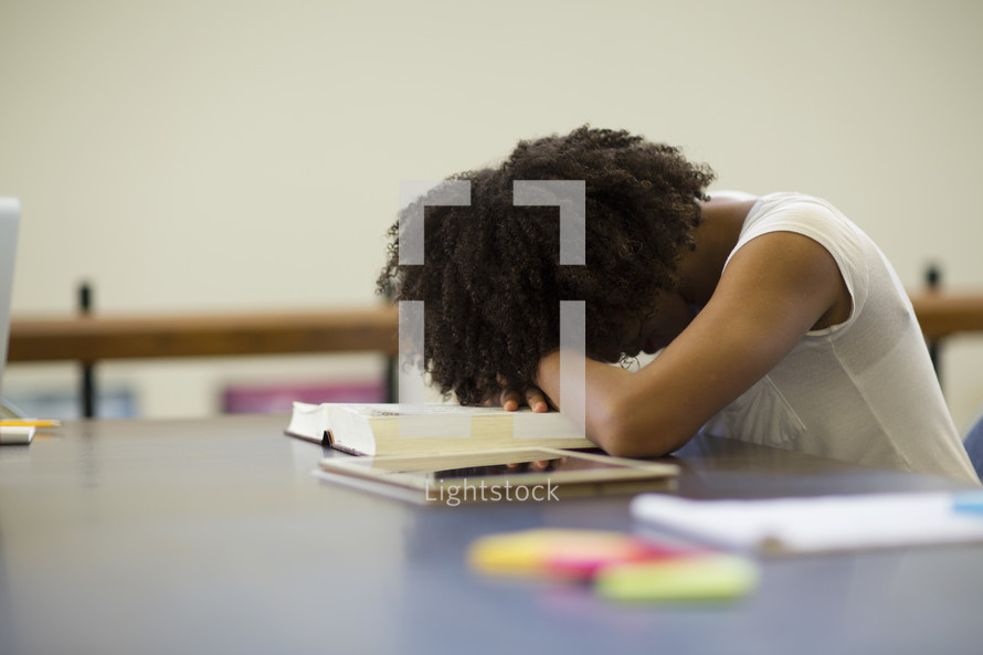 an exhausted woman with her head on a book in a library 