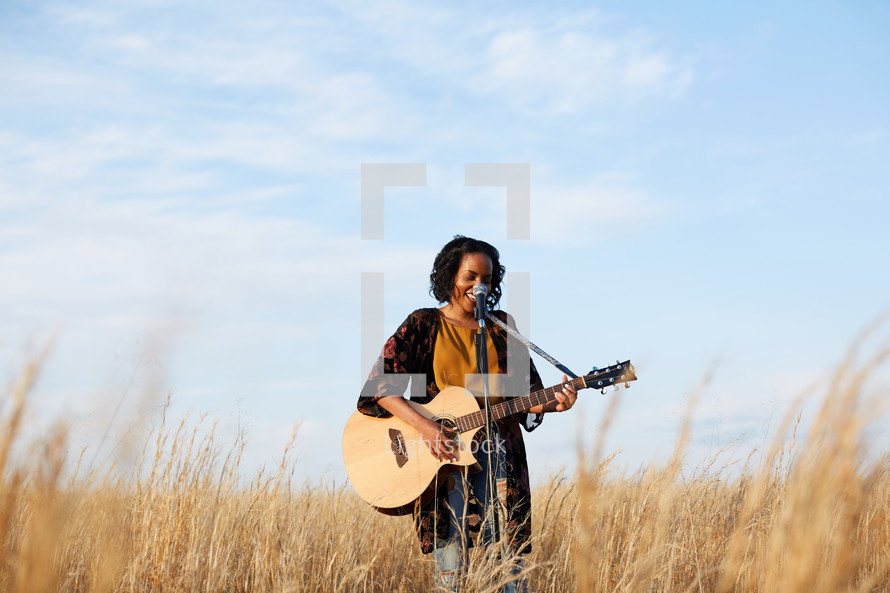 a woman standing in a field playing a guitar 