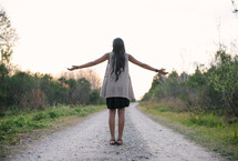 young woman standing on a dirt road with open arms 