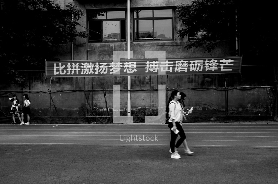 Young Chinese women walking along a road near a sign.