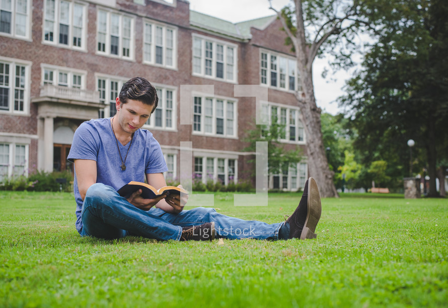 A man reads a Bible on a front lawn of an apartment complex.