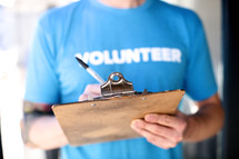 Person writing on a clipboard wearing a blue shirt with the word, "volunteer."