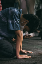 a boy kneeling in prayer wearing a facemask 