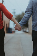 a couple holding hands walking down a street outdoors 