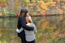 mother and daughter hugging by a lake in fall 