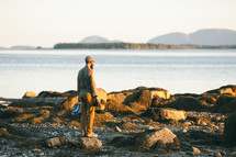 a man holding a camera standing on a shore 