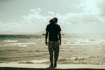 man standing on a wall along a shore 