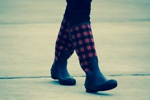 a woman walking on a sidewalk in plaid rain boots 