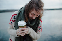 a teen girl holding a coffee cup and wearing a sweater and scarf 