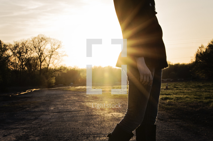 a torso of a woman standing on a dirt road in a sun flare 