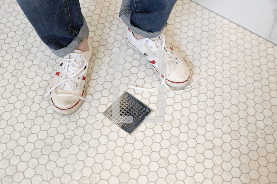 child's feet standing by a drain in a bathroom 