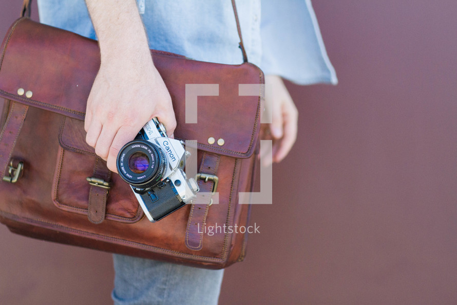 A man carrying a leather satchel and a camera.