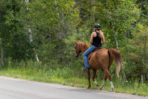 women riding a horse along the side of a country road 