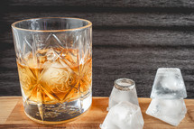 A glass of wiskey on the Rocks, on a black background, and a wooden table with wedding ring.