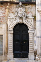 Arched black church doors in stone archway with Catholic emblem over