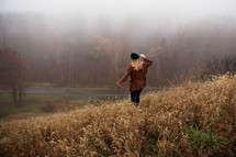a woman walking through tall brown grasses on a hill in fog 