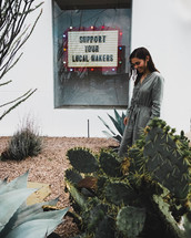 a woman standing on a sidewalk downtown standing in front of a sign that say support your local makers 