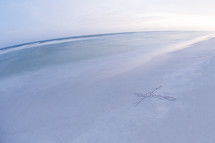 cross drawn in sand on a beach 
