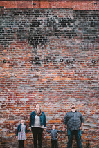 family standing in front of a brick wall holding hands and looking up 