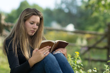 Girl reading a bible outside.