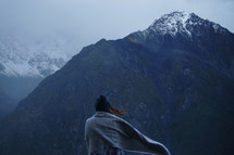 a woman wrapped in a blanket looking out at mountains 