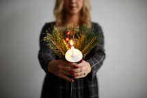 a woman holding a candle and Christmas greenery 