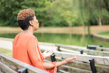 a woman sitting on a park bench with hands raised worshiping God 