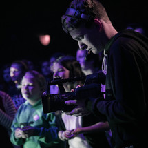 A young man shooting video of a youth worship service.