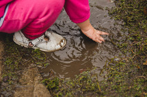 a toddler playing in a mud puddle 