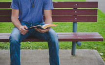 A man reads a Bible on a bench in a park