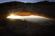 sunburst through a rock arch overlooking a canyon 
