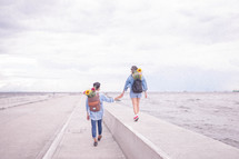a couple on a date with flowers in their backpacks walking on a bridge over the ocean 