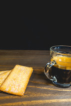 Glass cup of expresso with biscuits on a wooden table.