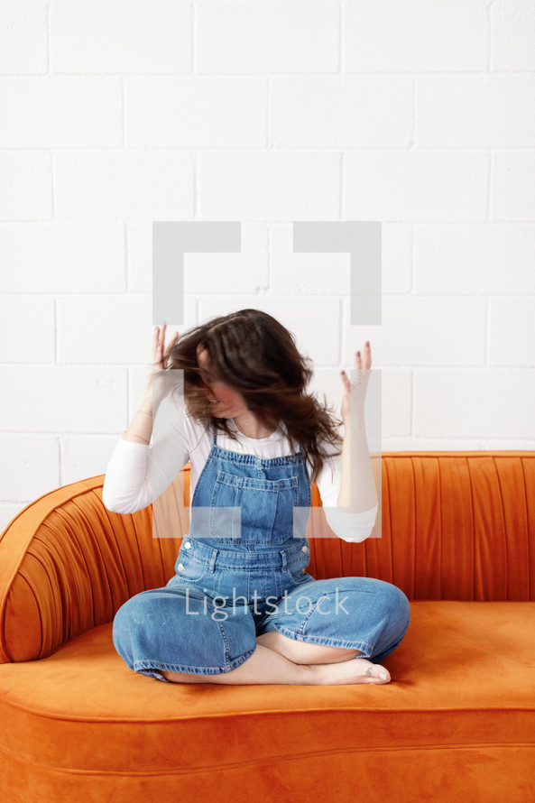 Woman shaking her hair back and forth on an orange couch 