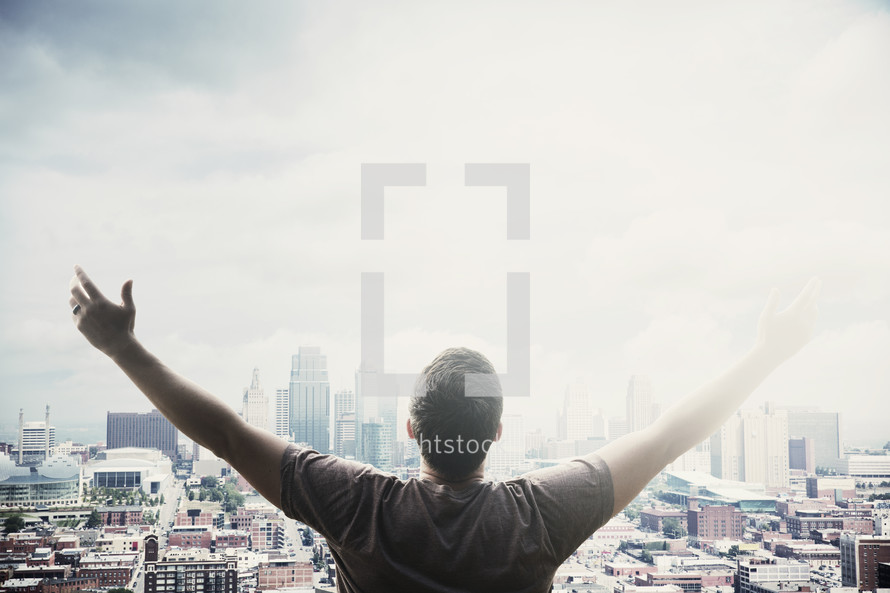 man standing in front of a city with raised arms 