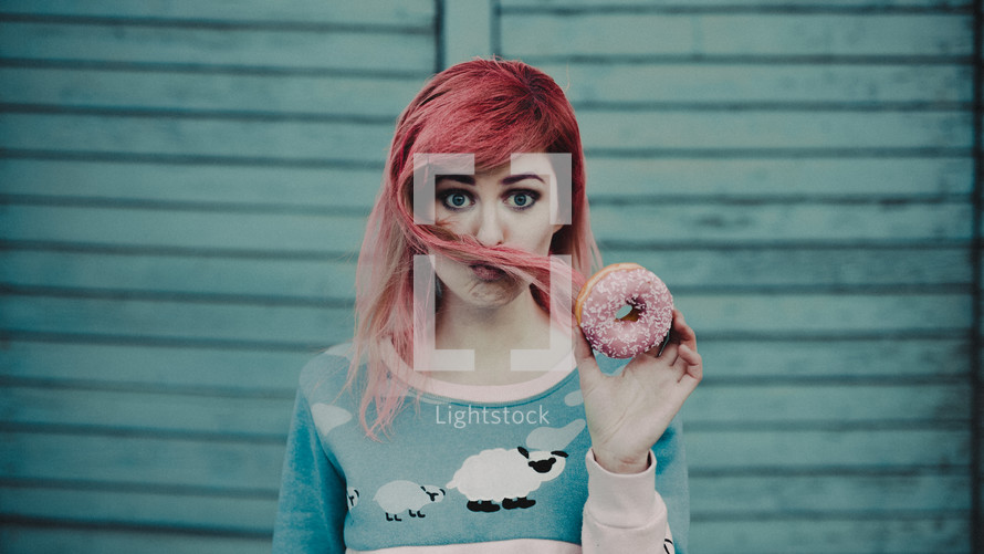a young woman with pink hair holding a donut 