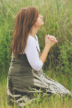 a young woman kneeling in a field praying 