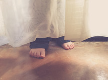 child's feet hiding behind a curtain 