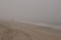 man walking on a beach in the fog 