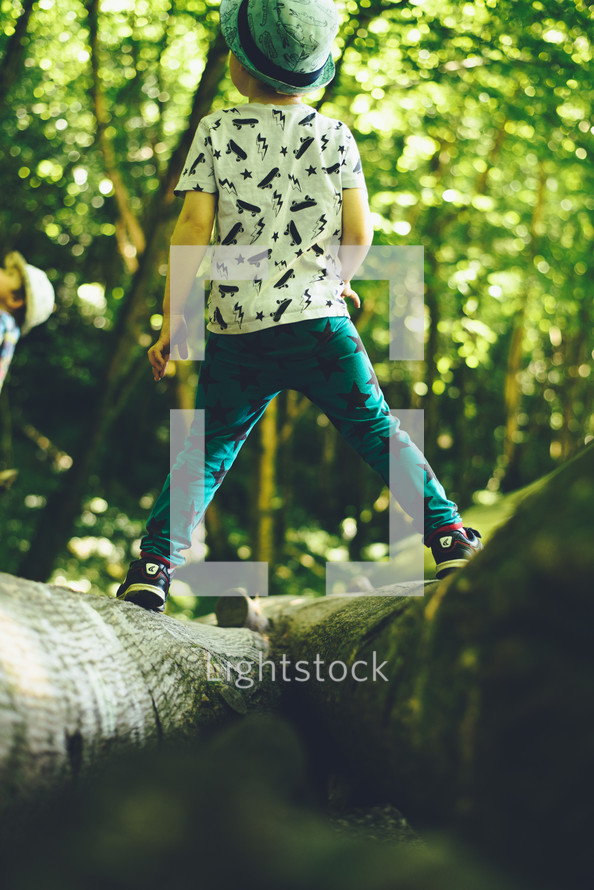 a toddler boy standing in the woods balancing between two trees 