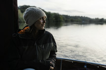 Woman on a river boat cruise, smiling and sailing, wearing a coat and wool hat, Norfolk Broads, outdoors exploring