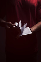 flipping through the pages of a Bible in a dark room.