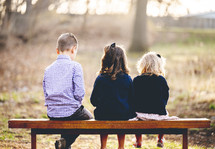 siblings sitting on a bench with backs to the camera 