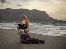 Woman reading a book on the beach and looking at the camera - You Are The Only One In the World